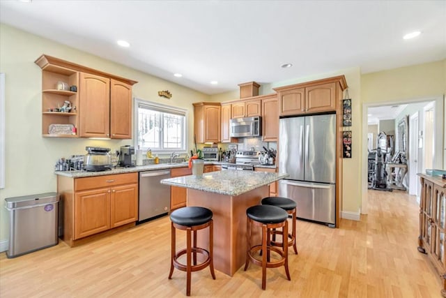 kitchen featuring light hardwood / wood-style flooring, stainless steel appliances, a kitchen breakfast bar, a kitchen island, and light stone counters