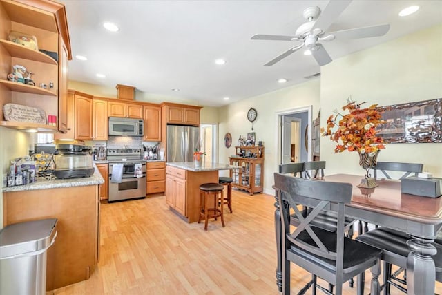 kitchen with a center island, a kitchen bar, stainless steel appliances, backsplash, and light hardwood / wood-style flooring