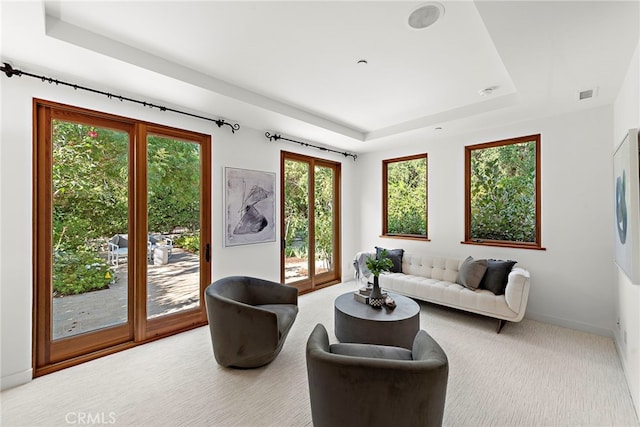 living area with carpet floors, visible vents, a tray ceiling, and baseboards