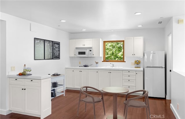 kitchen with white appliances, white cabinetry, light countertops, decorative backsplash, and dark wood-style floors