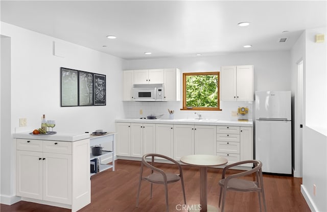 kitchen with decorative backsplash, white cabinetry, dark wood-style flooring, and white appliances