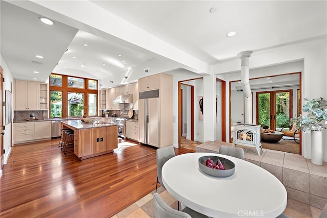 dining space featuring light wood-type flooring, a wood stove, vaulted ceiling, and recessed lighting