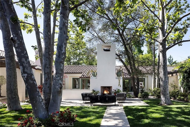 rear view of property featuring a patio, a chimney, stucco siding, a lit fireplace, and a tiled roof