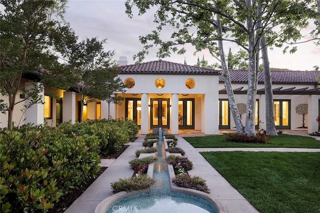 rear view of house featuring a tiled roof, french doors, stucco siding, and a lawn