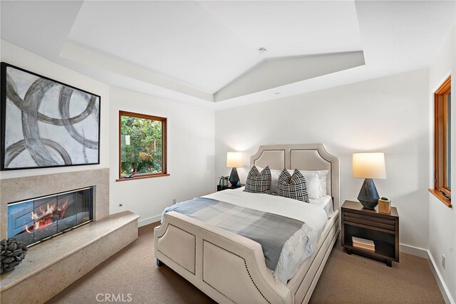 carpeted bedroom featuring vaulted ceiling, a premium fireplace, baseboards, and a raised ceiling