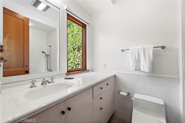 bathroom with visible vents, toilet, wainscoting, a tile shower, and vanity