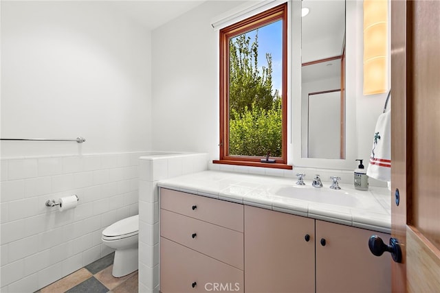 bathroom featuring a healthy amount of sunlight, toilet, tile walls, and vanity