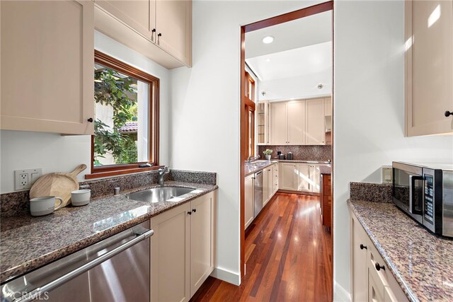 kitchen featuring appliances with stainless steel finishes, dark wood-type flooring, a sink, stone counters, and backsplash