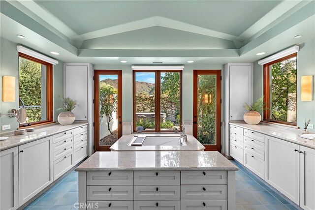 kitchen featuring lofted ceiling, a kitchen island, white cabinetry, and light stone counters