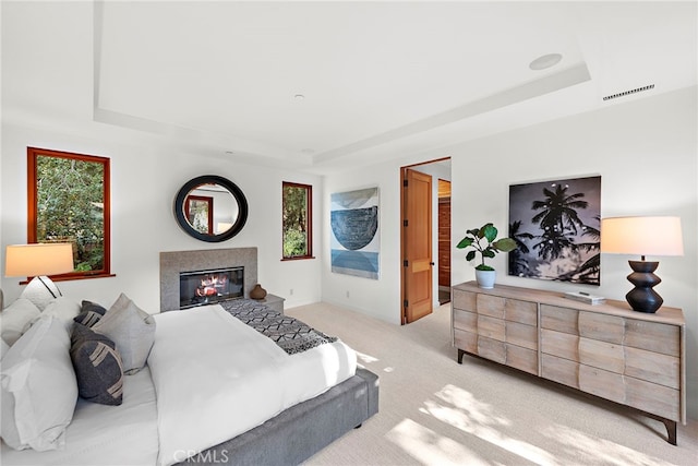 bedroom with light colored carpet, visible vents, multiple windows, a raised ceiling, and a glass covered fireplace