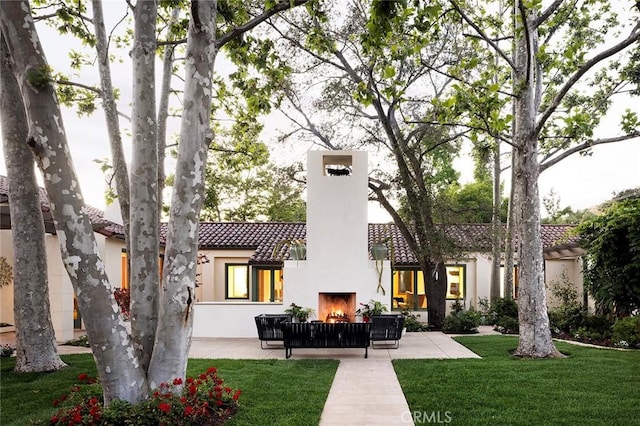 rear view of house with exterior fireplace, a patio area, and a lawn