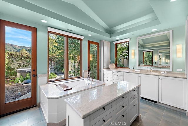 kitchen with light stone counters, a center island, white cabinetry, vaulted ceiling, and a sink