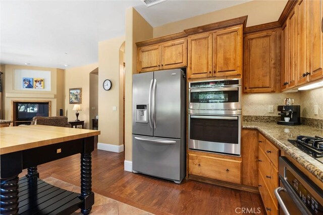 kitchen with tasteful backsplash, dark hardwood / wood-style flooring, stainless steel appliances, and light stone counters