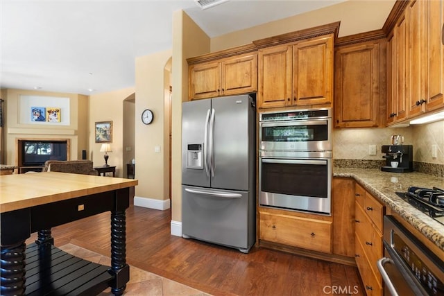 kitchen with arched walkways, appliances with stainless steel finishes, backsplash, dark wood-style floors, and brown cabinetry