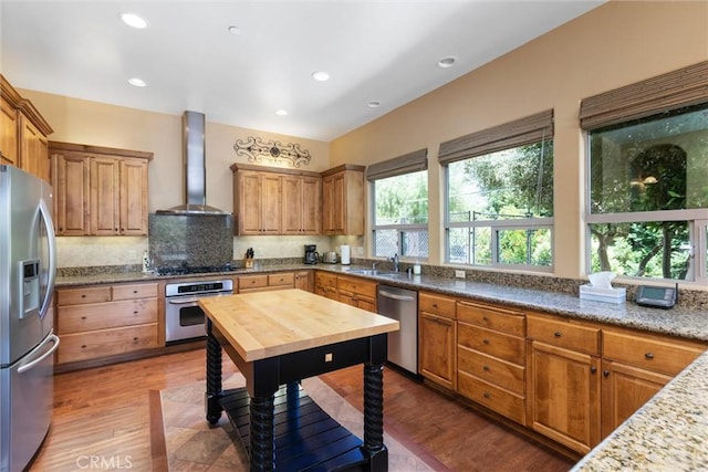 kitchen featuring wall chimney exhaust hood, backsplash, wood finished floors, stainless steel appliances, and a sink