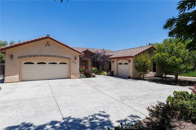 mediterranean / spanish home with concrete driveway, a tiled roof, an attached garage, and stucco siding