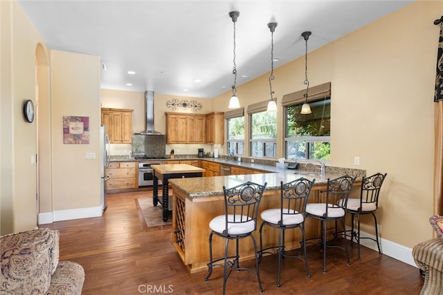 kitchen featuring wall chimney exhaust hood, kitchen peninsula, dark hardwood / wood-style flooring, stainless steel appliances, and decorative light fixtures