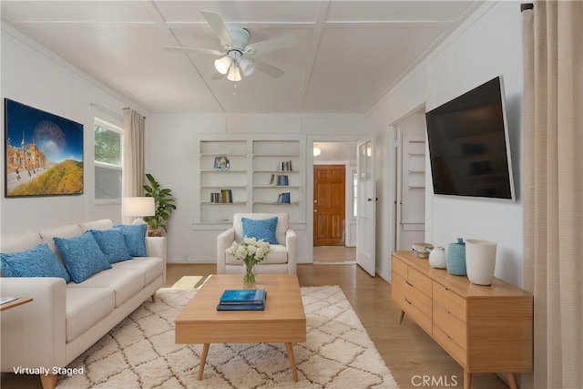 living room featuring light hardwood / wood-style floors, built in shelves, crown molding, and ceiling fan