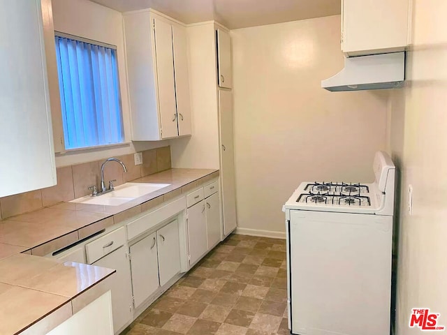 kitchen with white range with gas stovetop, white cabinets, sink, and tile counters