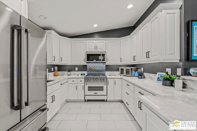 kitchen featuring high quality appliances, white cabinetry, lofted ceiling, light stone counters, and light tile patterned floors