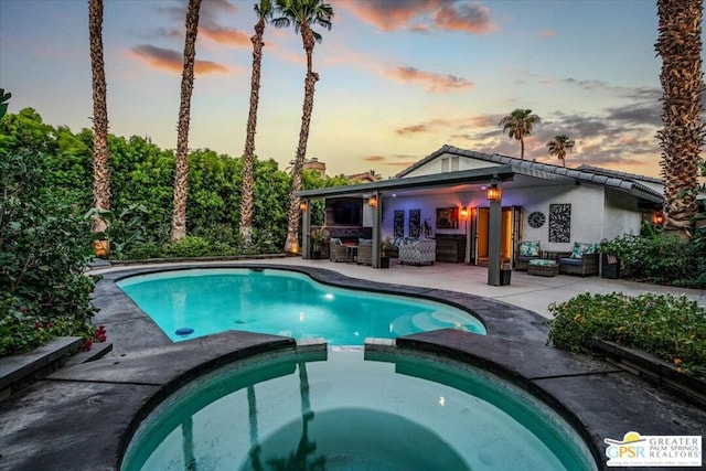 pool at dusk with an in ground hot tub, a patio area, an outdoor bar, and an outdoor hangout area