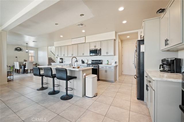 kitchen with light stone counters, a kitchen bar, a center island with sink, appliances with stainless steel finishes, and light tile patterned floors