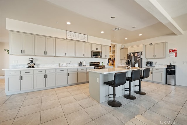 kitchen featuring an island with sink, sink, light tile patterned floors, appliances with stainless steel finishes, and a breakfast bar area