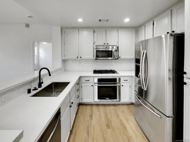 kitchen with white cabinetry, sink, light hardwood / wood-style floors, and appliances with stainless steel finishes