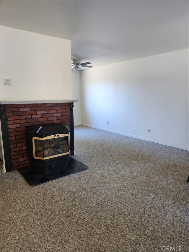 unfurnished living room featuring a wood stove, dark carpet, and ceiling fan