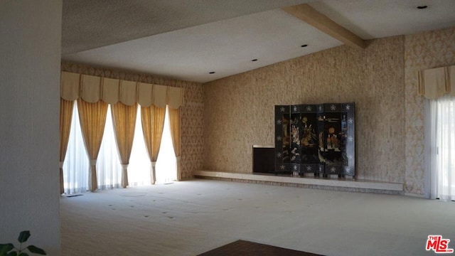 unfurnished living room featuring beamed ceiling, carpet flooring, and a healthy amount of sunlight