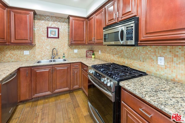 kitchen featuring appliances with stainless steel finishes, dark hardwood / wood-style floors, light stone counters, and sink