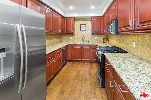 kitchen featuring backsplash, sink, light stone countertops, light hardwood / wood-style floors, and stainless steel appliances