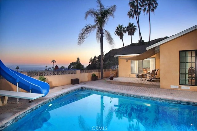 pool at dusk featuring a patio and a water slide