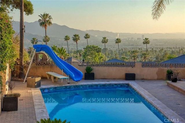 pool at dusk featuring a mountain view, a patio area, and a water slide