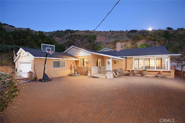 back house at dusk featuring a garage and a patio area