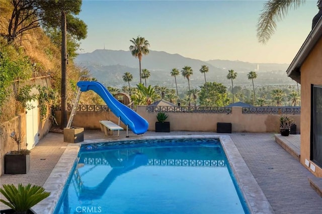 view of swimming pool with a patio area, a mountain view, and a water slide