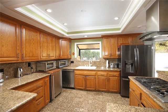 kitchen with appliances with stainless steel finishes, a raised ceiling, wall chimney exhaust hood, and sink