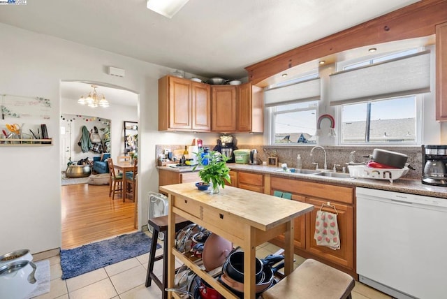 kitchen with light wood-type flooring, dishwasher, sink, an inviting chandelier, and backsplash