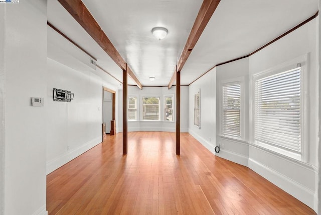 empty room with light hardwood / wood-style floors and beam ceiling