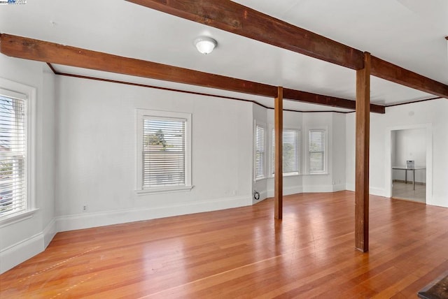 empty room with beamed ceiling, light hardwood / wood-style flooring, and plenty of natural light