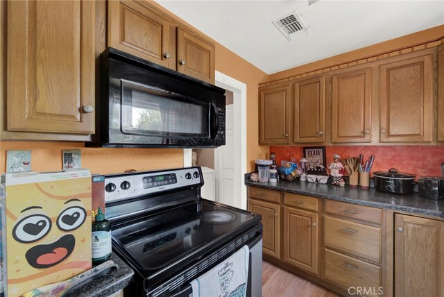 kitchen with black appliances, dark stone countertops, and light wood-type flooring