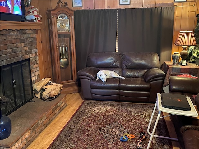 living room featuring a brick fireplace, hardwood / wood-style flooring, and wooden walls