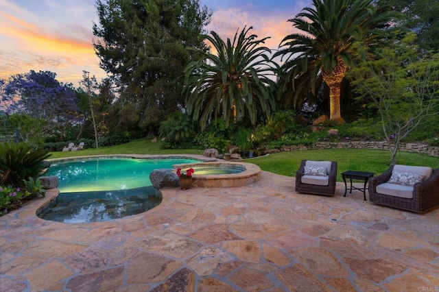 pool at dusk featuring an in ground hot tub, a yard, and a patio