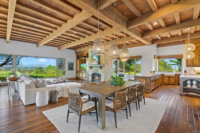 dining area with hardwood / wood-style floors, beamed ceiling, a stone fireplace, and wooden ceiling