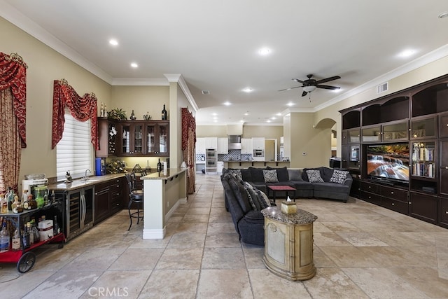 living room featuring indoor wet bar, ornamental molding, and ceiling fan