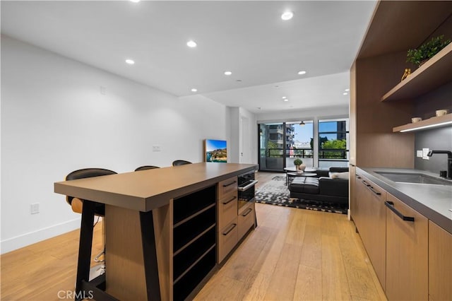 kitchen with sink, stainless steel oven, a kitchen bar, light brown cabinetry, and light wood-type flooring