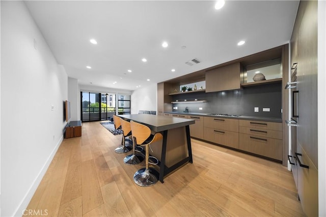 kitchen with decorative backsplash, a breakfast bar, cooktop, a center island, and light hardwood / wood-style floors