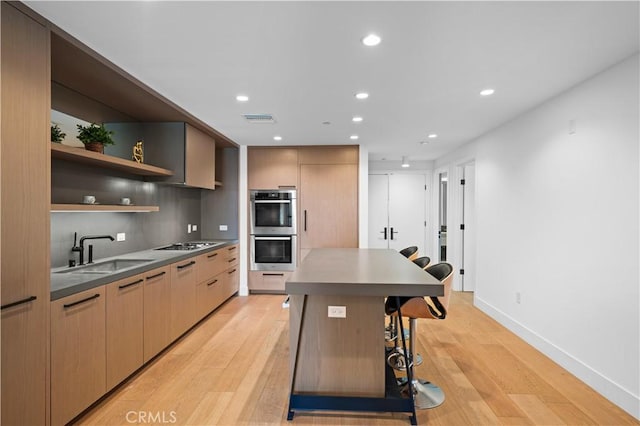 kitchen featuring light wood-type flooring, double oven, sink, a center island, and a breakfast bar area