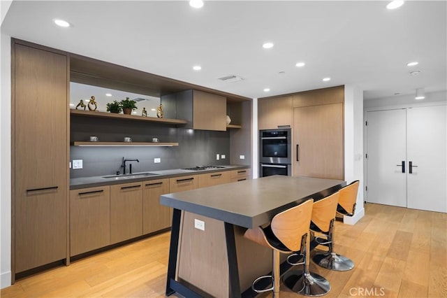 kitchen featuring gas stovetop, sink, double oven, and light hardwood / wood-style flooring