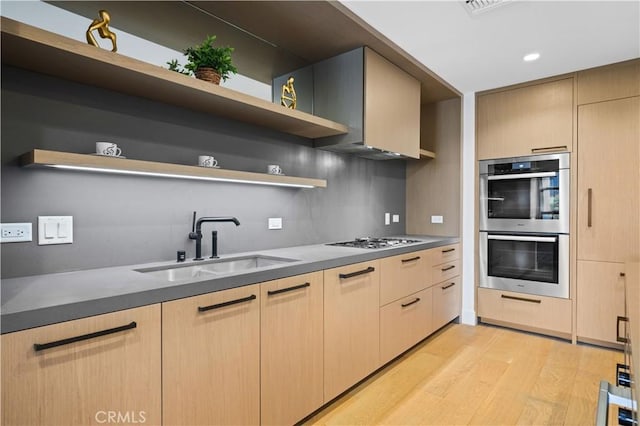 kitchen featuring light brown cabinets, sink, gas stovetop, light wood-type flooring, and double oven